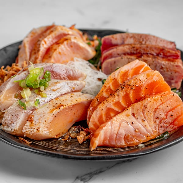 A black plate filled with various cuts of seared salmon and tuna sashimi, garnished with scallions.
