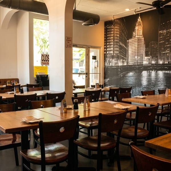 Spacious restaurant dining room with wooden tables and chairs, a long booth, and a city mural.