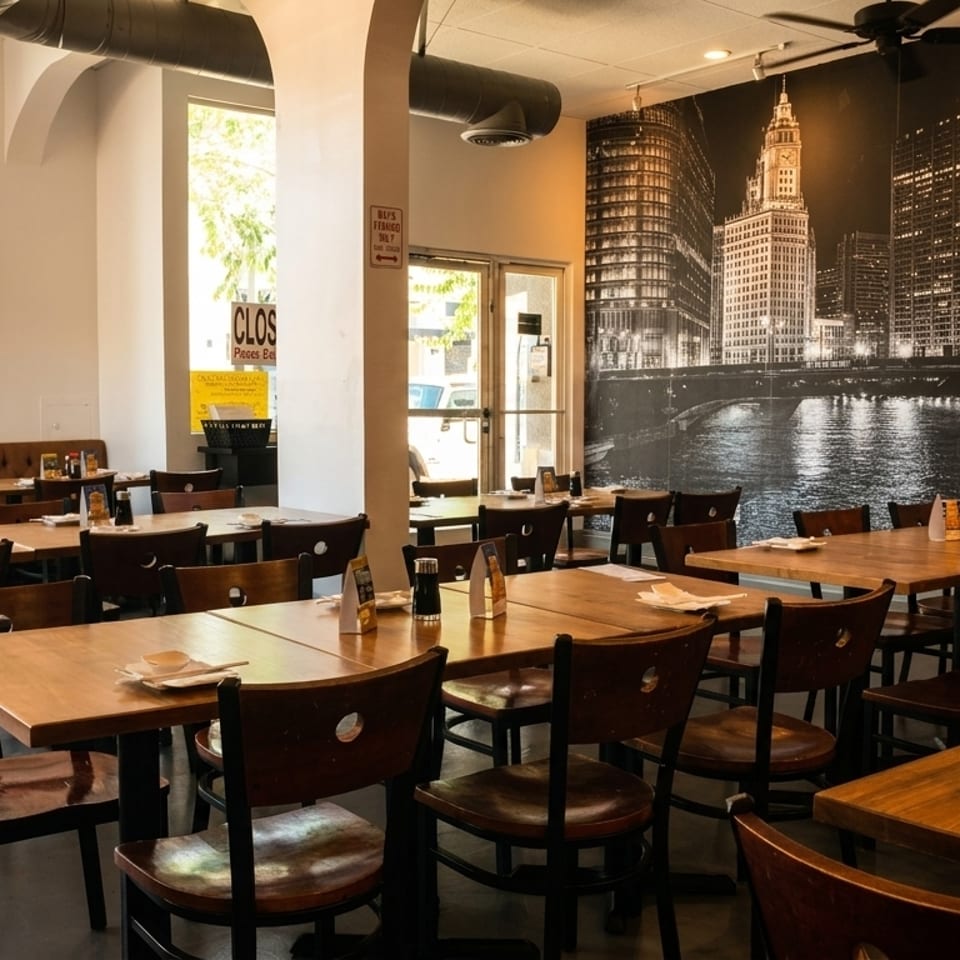 Spacious restaurant dining room with wooden tables and chairs, a long booth, and a city mural.