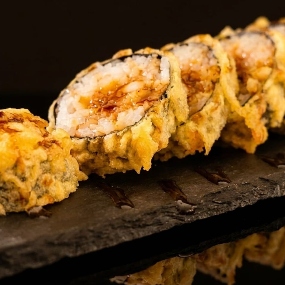 Tempura-fried sushi rolls with a sweet sauce drizzle, served on a dark slate board.