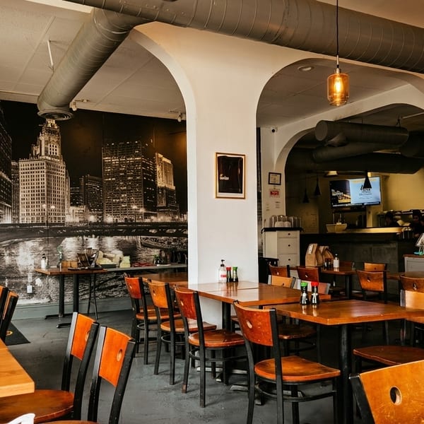 Interior of a restaurant with wooden tables and chairs, a city mural, and an open kitchen.
